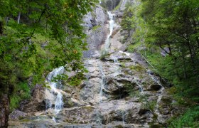 A waterfall flows over rocks in a wooded area.