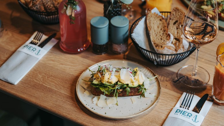 Ein gedeckter Tisch mit einem belegten Brot, Getränken und Besteck im Restaurant Pier 4.