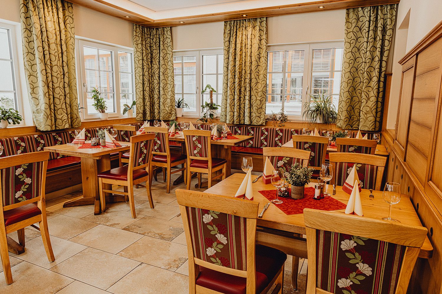 Gemütliches Restaurant mit Holzmöbeln, dekorierten Tischen und Pflanzen am Fenster.