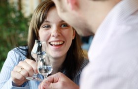 Zwei Personen stoßen mit Schnapsgläsern an und lächeln.