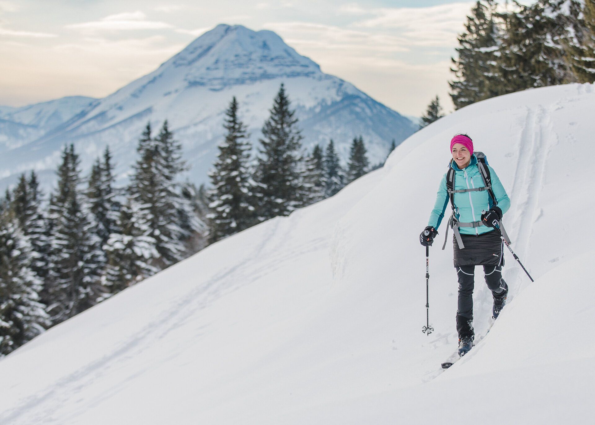 Eine Frau genießt die frische Winterluft auf ihrer Skitour und lässt sich von der atemberaubenden Aussicht auf die schneebedeckten Berge verzaubern. Die unberührte Schneelandschaft und die majestätischen Tannen schaffen eine friedliche Atmosphäre, die zum Verweilen einlädt.