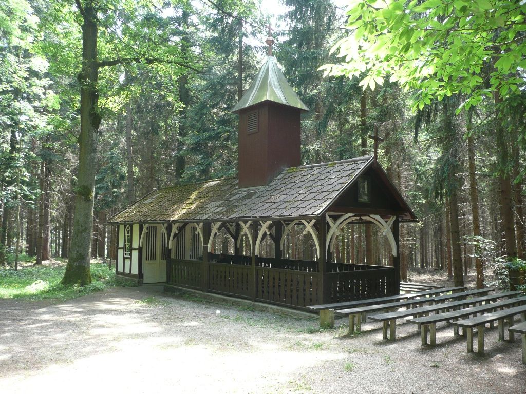 Eine kleine Kapelle im Wald mit Holzbänken im Freien.
