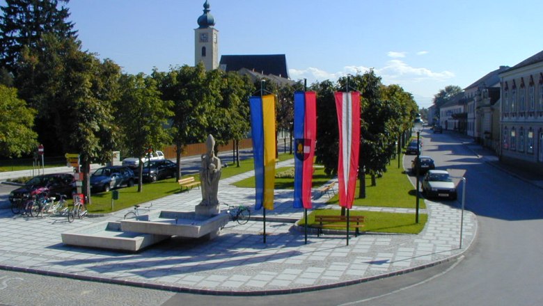 Platz in Ruprechtshofen mit Kirche, Statuen und Fahnen.