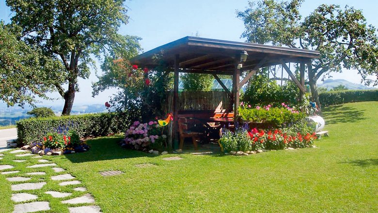 Oberschönbichl farm, © Oberschönbichl A pavilion on a green lawn with colorful flowers and trees in the background.