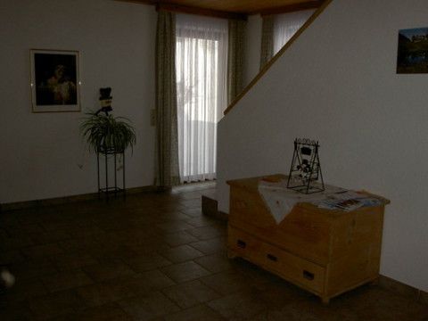 Innenansicht eines Wohnbereichs mit Holzkiste, Pflanze und Treppe.