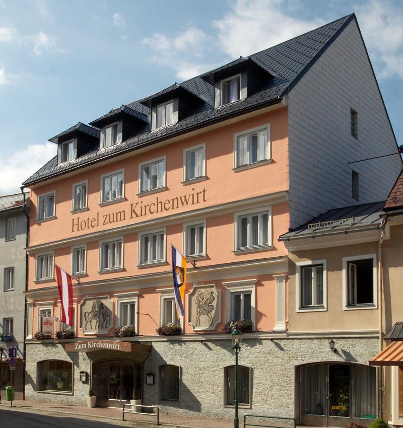 Fassade des Hotels zum Kirchenwirt mit Fahnen und blauer Himmel.