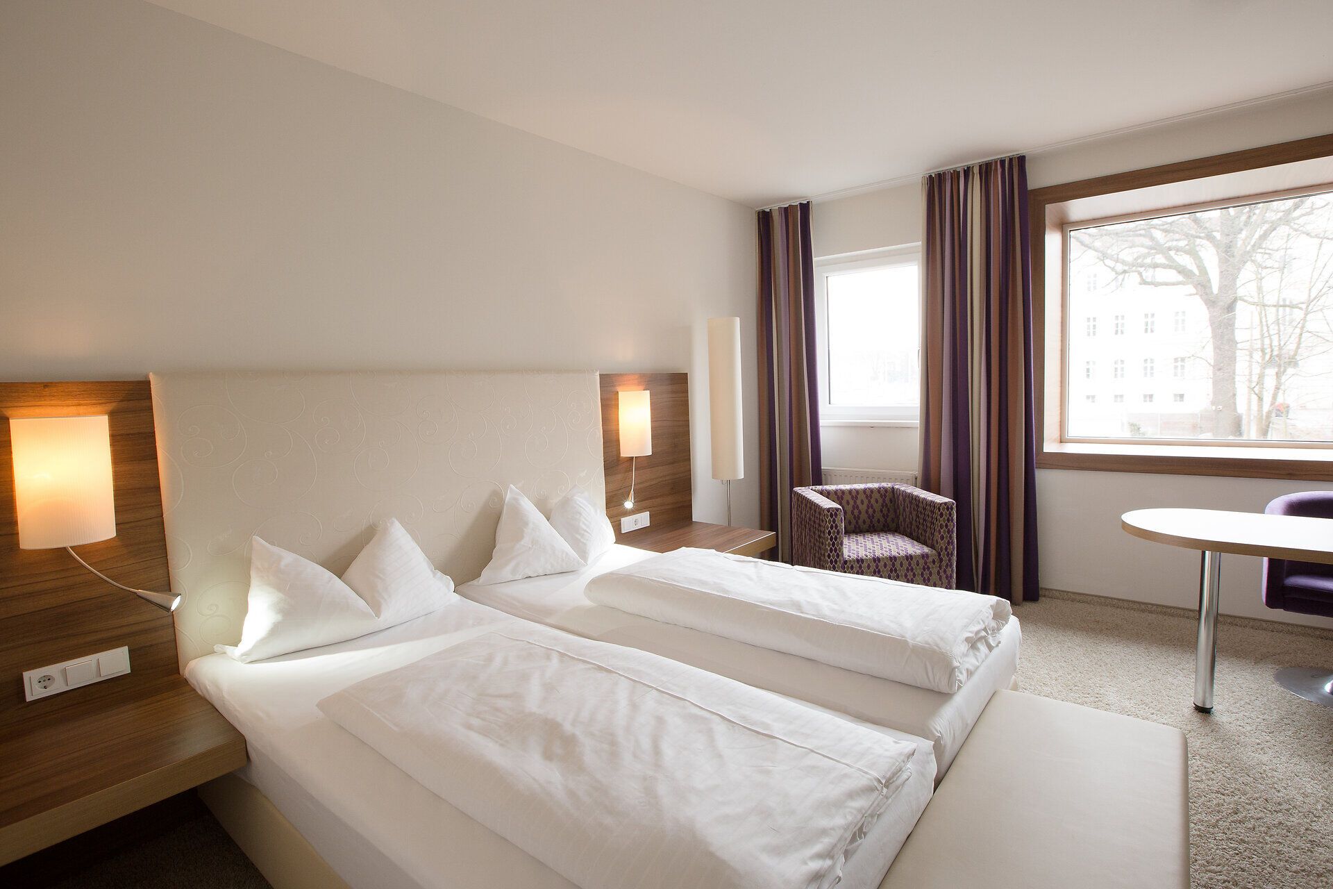 In einem modernen Hotelzimmer erwartet Sie eine harmonische Atmosphäre mit sanften Farben und stilvollem Design. Die großen Fenster bieten einen Blick auf die umliegende Stadtlandschaft und laden dazu ein, die Ruhe und den Komfort zu genießen. Ideal für Reisende, die nach einem erholsamen Rückzugsort suchen.