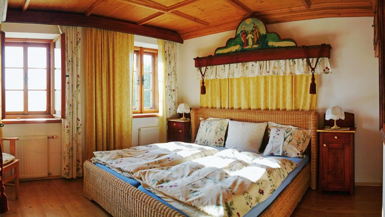 Gemütliches Schlafzimmer mit Holzmöbeln und Doppelbett, dekoriert mit floralen Mustern und gelben Vorhängen.