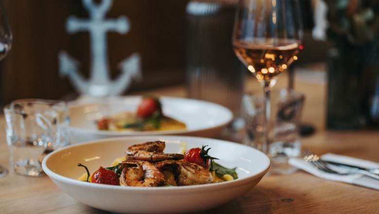A plate of prawns and vegetables on a table, with a glass of wine next to it.