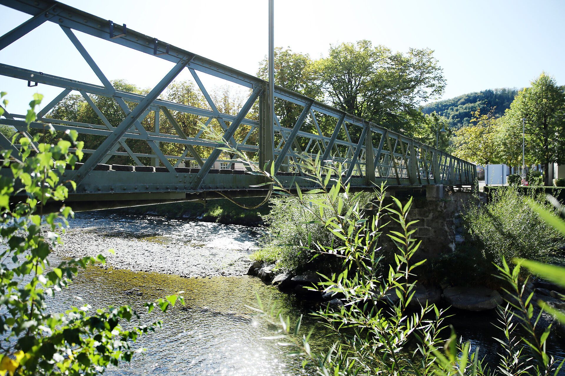 Die sanfte Brise streicht über die glitzernde Oberfläche des Wassers, während die Brücke majestätisch über den Fluss führt. Umgeben von üppigem Grün und dem sanften Rauschen der Natur, lädt dieser Ort zum Verweilen und Entspannen ein. Hier, wo Wasser und Landschaft harmonisch verschmelzen, erleben Wanderer die Schönheit der Umgebung in vollen Zügen.