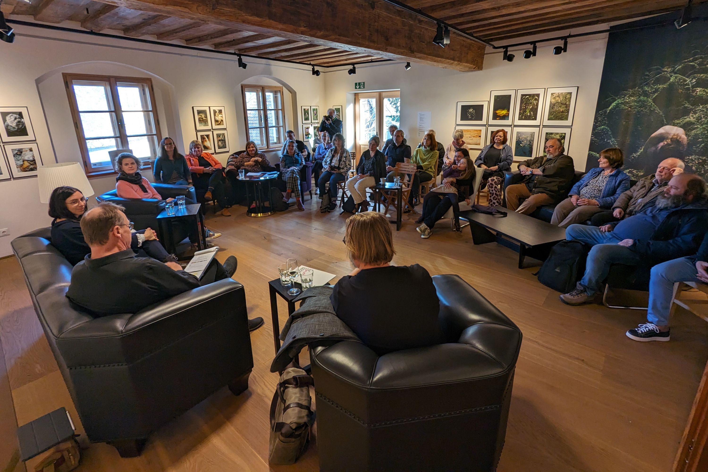 Menschen sitzen in einem Raum einer Kunstgalerie und führen ein Gespräch.