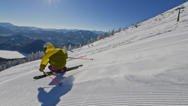 Skifahrer auf einer Piste mit Blick auf den Erlaufsee und Berge im Hintergrund.