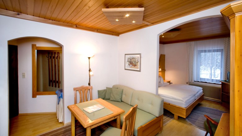 Gem&uuml;tliches Hotelzimmer mit Holzm&ouml;beln, Esstisch, Sofa und Doppelbett.