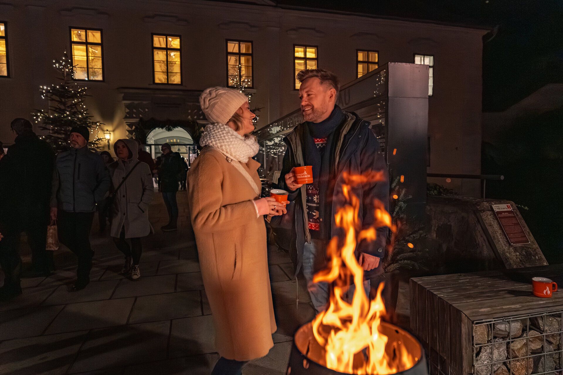Gäste wärmen sich am Feuerkorb auf dem Hof.