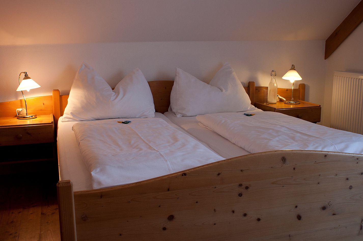 Gemütliches Doppelbett in einem Landgasthofzimmer mit Holzrahmen und Nachttischen, beleuchtet von zwei Tischlampen.