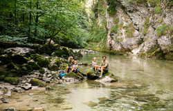 Ein erfrischender Moment in der Natur, wo eine Familie am Ufer eines glasklaren Baches sitzt. Umgeben von üppigem Grün und sanften Felsen, genießen sie die Ruhe und die Schönheit des Naturparks Ötscher Tormäuer.