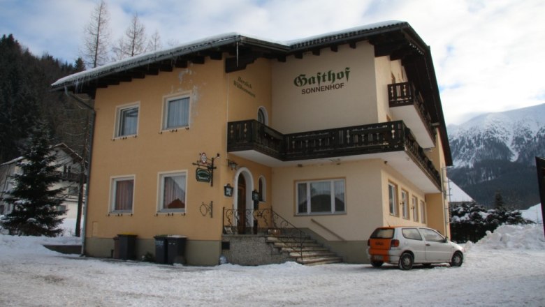 Ein gelbes Gebäude mit der Aufschrift 'Gasthof Sonnenhof' im Schnee, umgeben von Bergen.