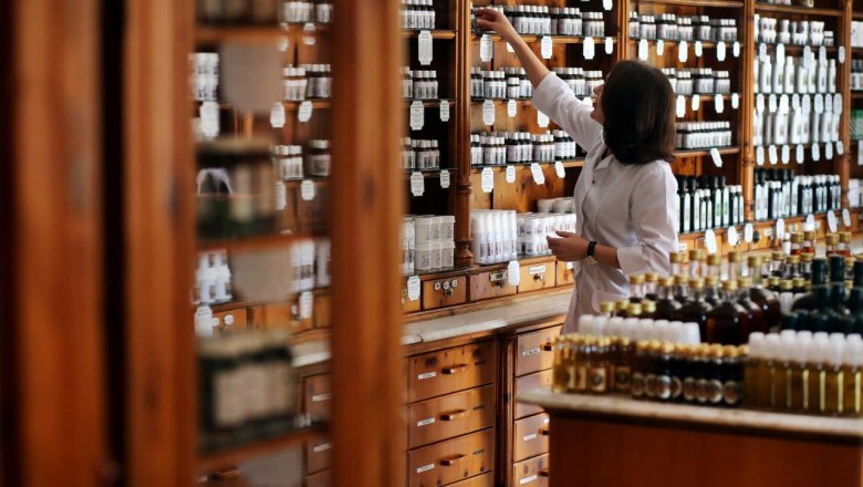 A pharmacist in a traditional pharmacy store, surrounded by wooden shelves full of bottles and jars.