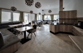 Moderner Fr&uuml;hst&uuml;cksraum mit Holzm&ouml;beln, grauen Polstern und dekorativen Lampen.