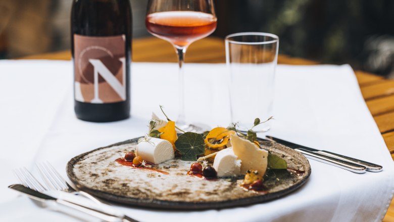 Egy t&aacute;ny&eacute;r sajt &eacute;s k&ouml;ret, egy poh&aacute;r roz&eacute; bor &eacute;s egy &uuml;veg bor az asztalon.