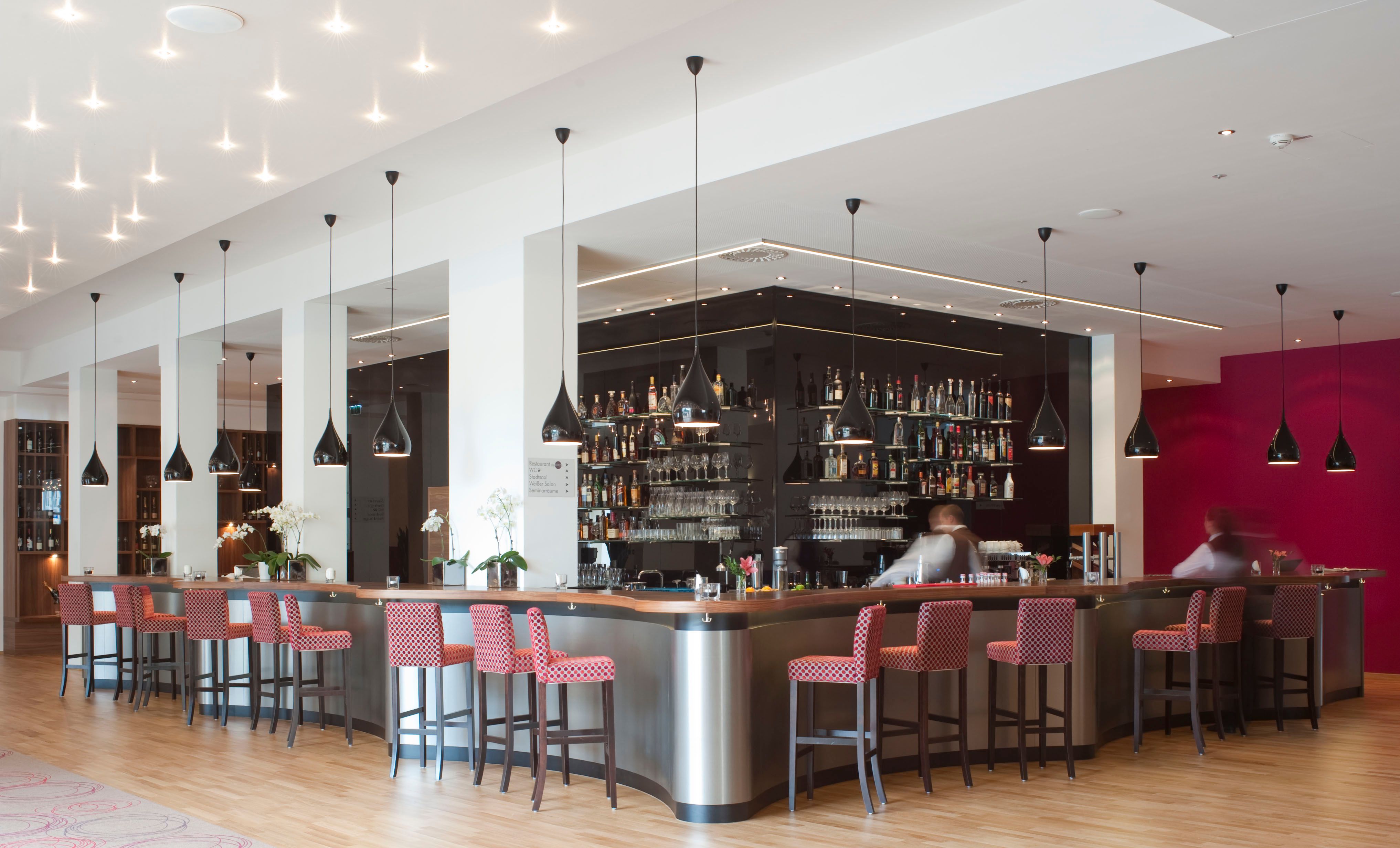 Moderne Hotelbar mit roten Stühlen und schwarzen Hängelampen.