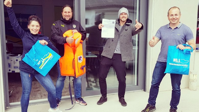 Vier Personen stehen vor einem Gebäude, halten Taschen und eine Schwimmweste, lächeln und zeigen Daumen hoch.