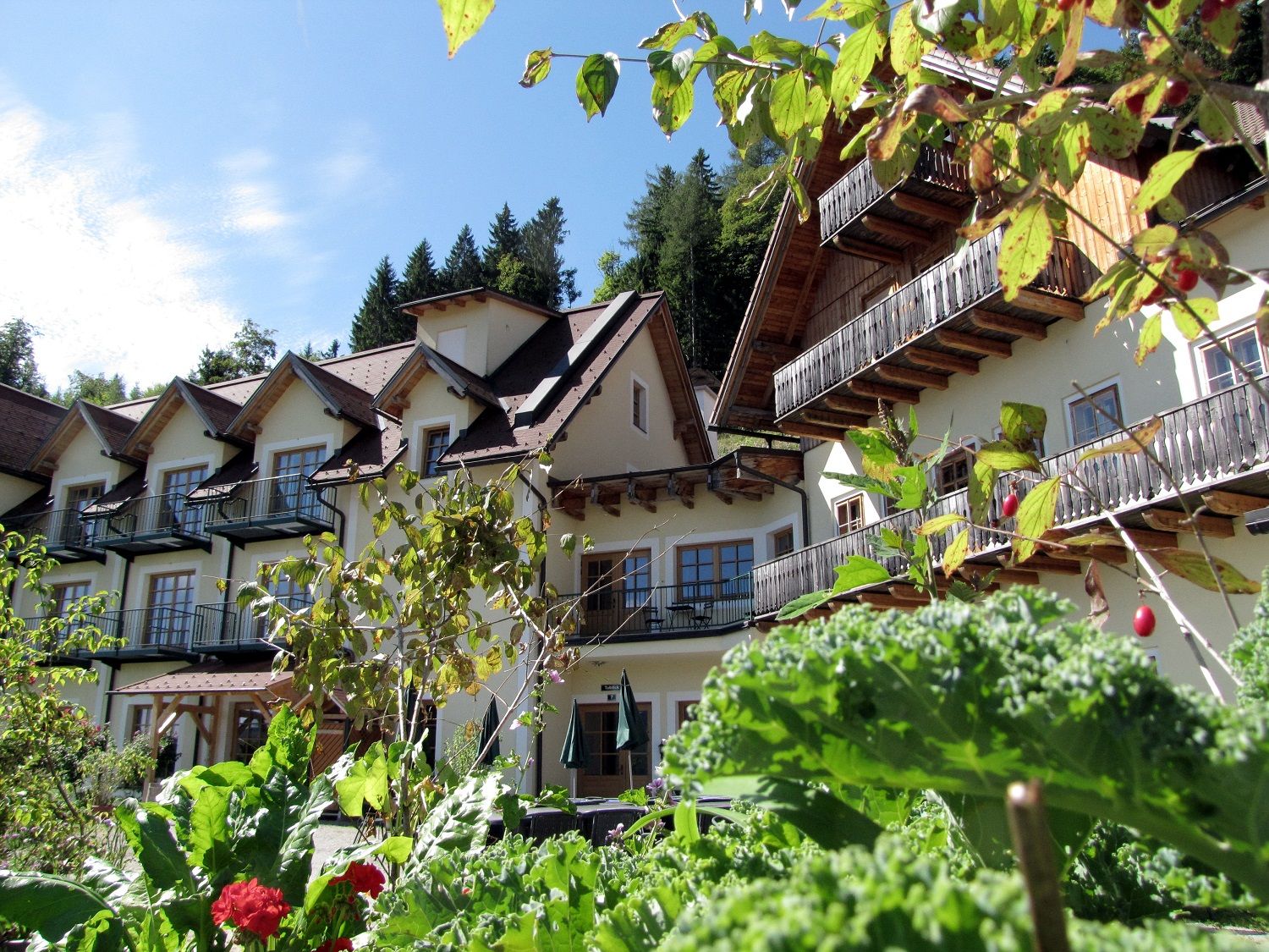 Ein Gebäude im alpinen Stil mit Balkonen, umgeben von üppigem Grün und Pflanzen.