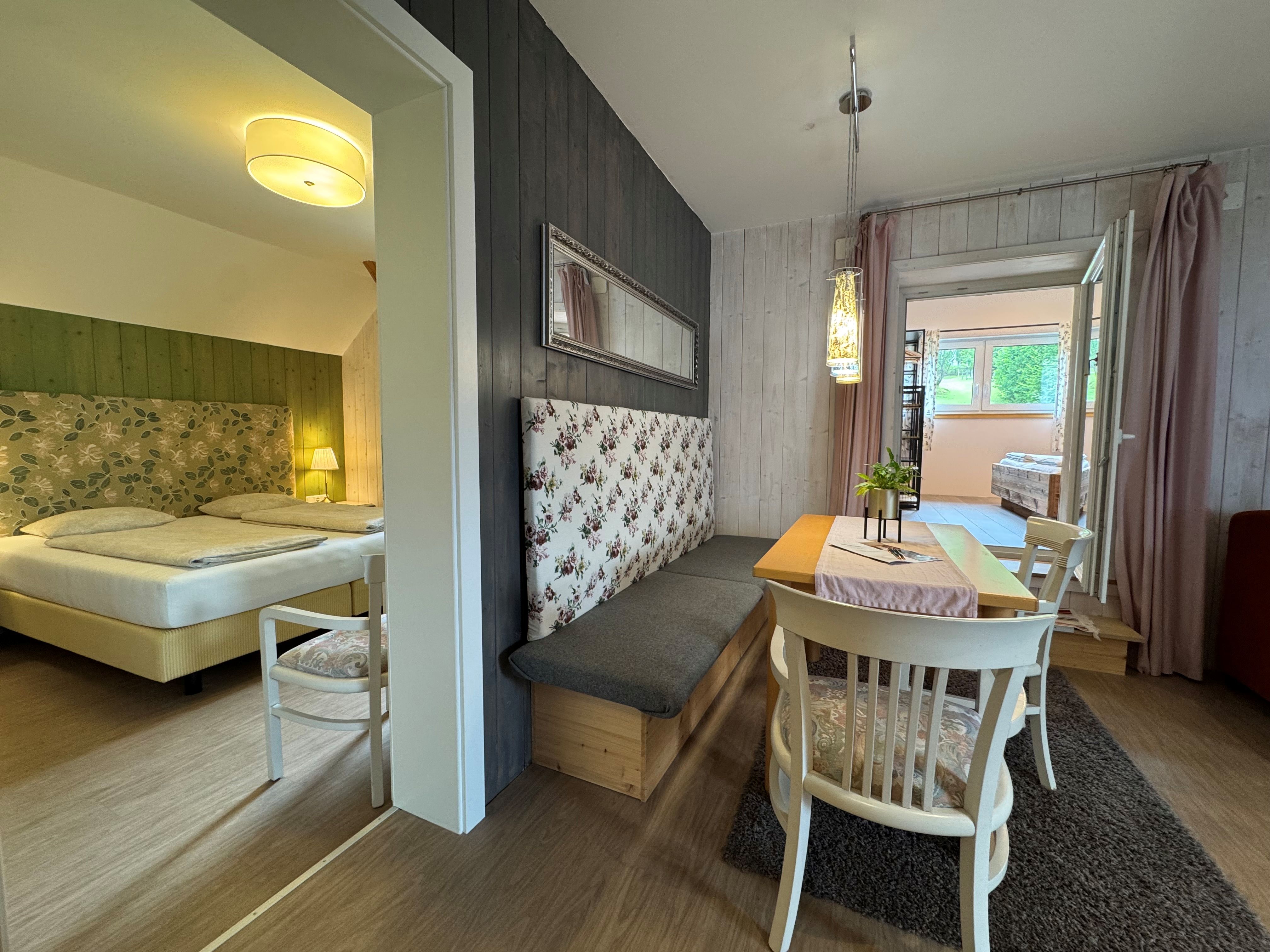 Innenansicht eines gemütlichen Zimmers mit Esstisch, Stühlen und einem Bett im Hintergrund.