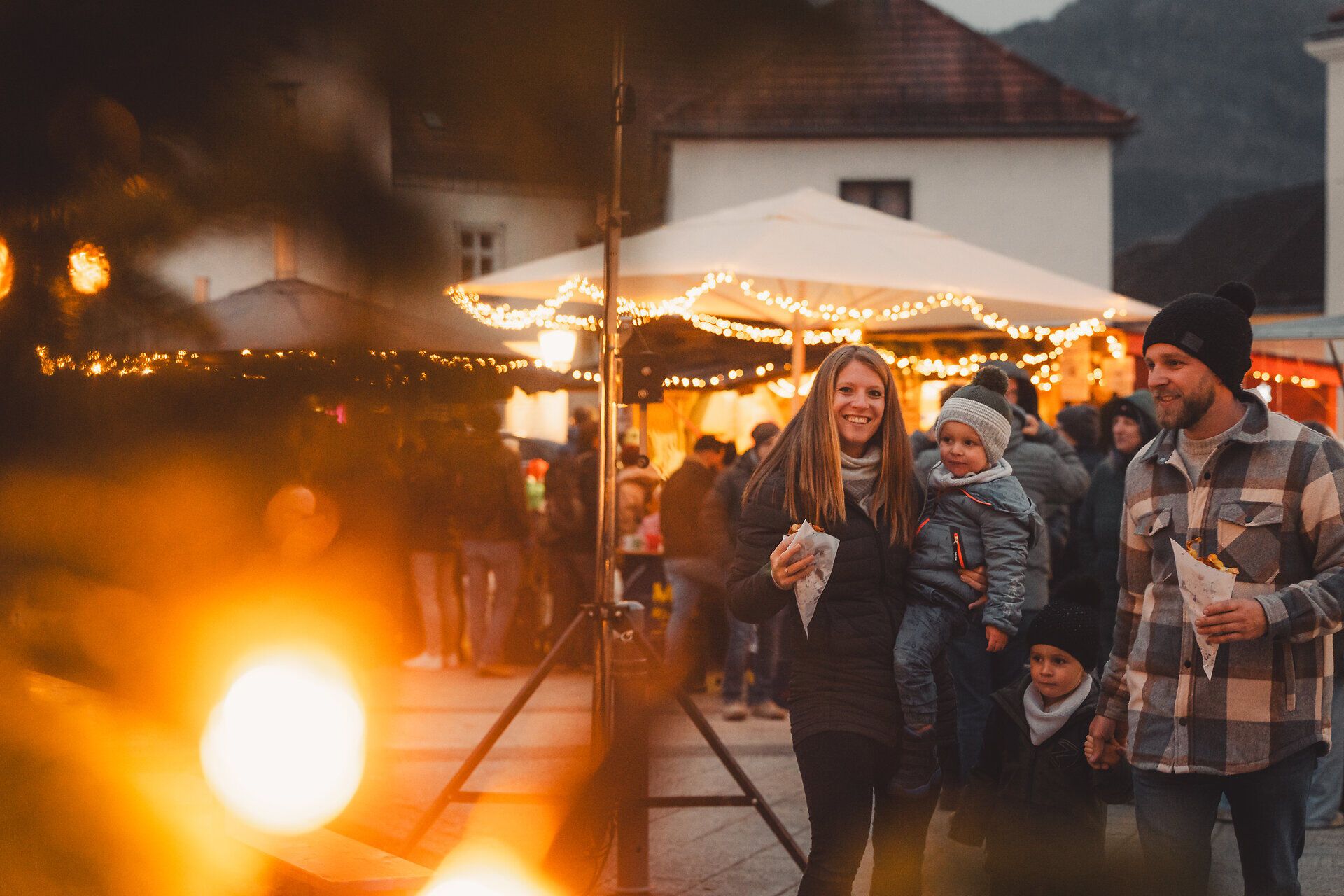 Familie am Adventmarkt der Flammenden Weihnacht in Scheibbs, im Hintergrund festliche Beleuchtung.