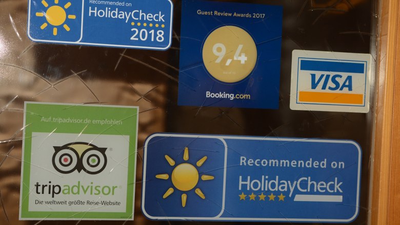 Aufkleber von HolidayCheck, Booking.com, TripAdvisor und Visa auf einer Glasoberfläche.