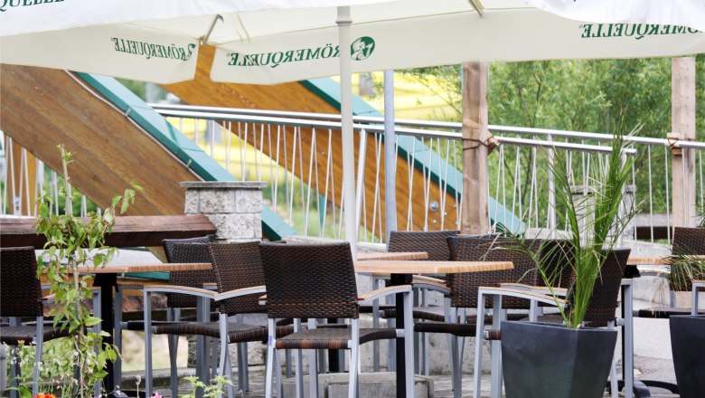 Gemütliche Terrasse mit Tischen, Stühlen und Sonnenschirmen.