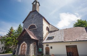 Pfarrkirche Josefsberg mit steinverkleideter Fassade und Turm unter blauem Himmel.