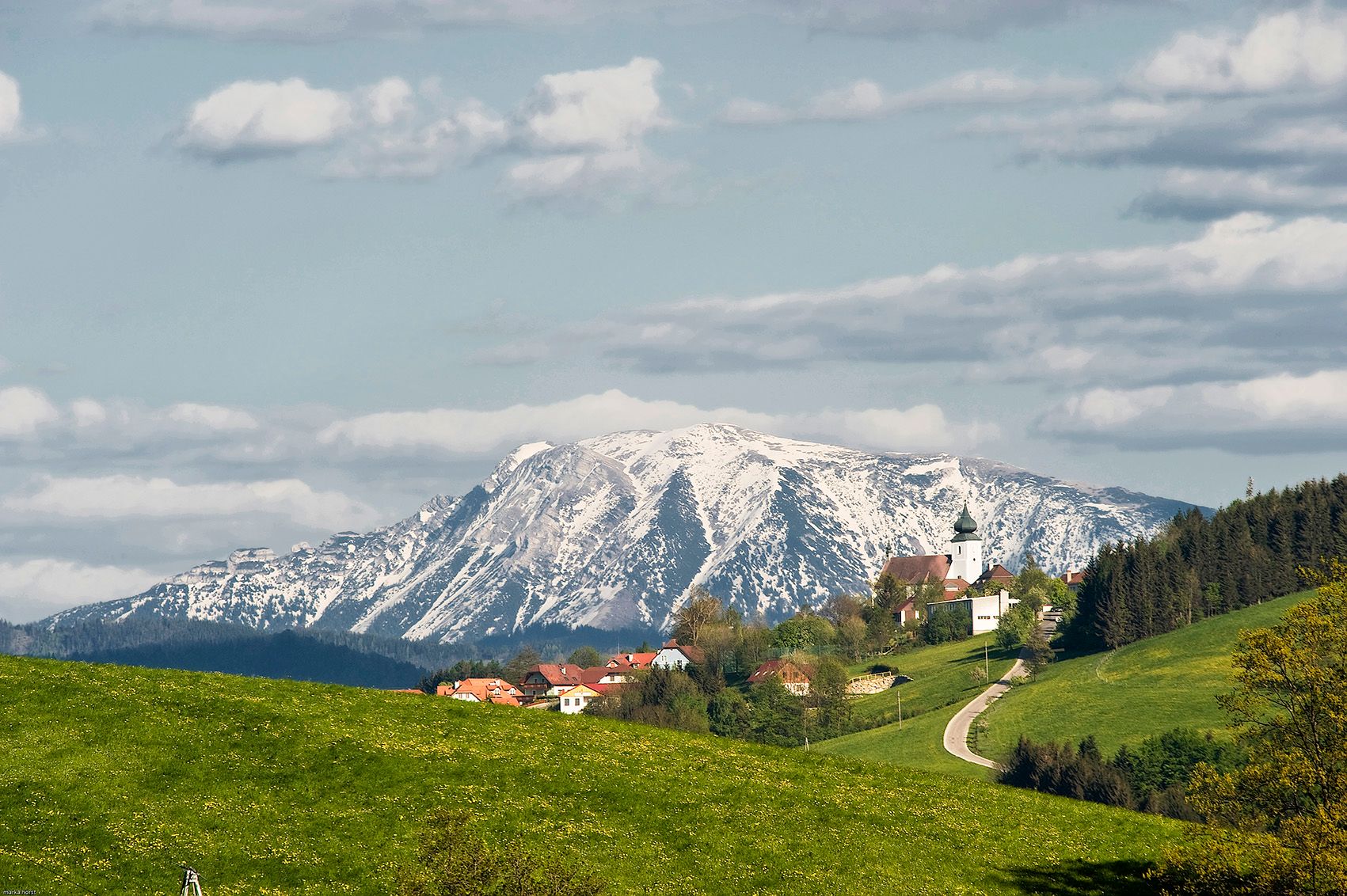 Blick auf St. Leonhard am Walde mit schneebedecktem Berg im Hintergrund.