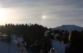 Teleskope auf einer verschneiten Bergstation mit Sonnenhalo im Hintergrund.