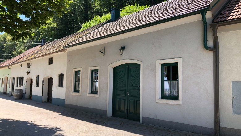 Exterior view of a traditional wine tavern with white walls and green gate, surrounded by trees.