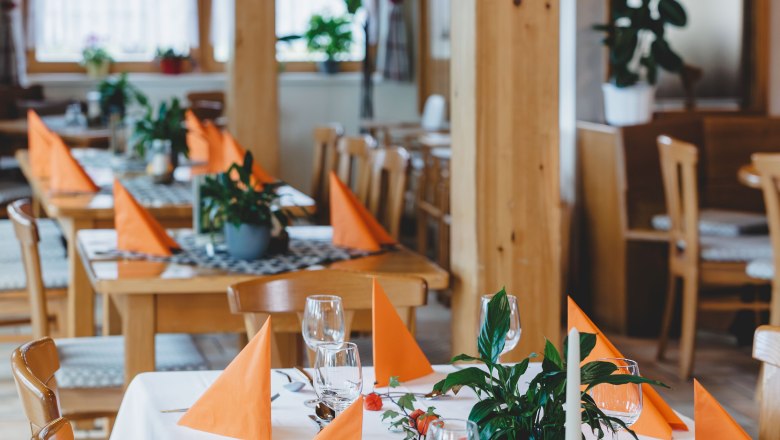 Ein festlich gedeckter Tisch in einem Restaurant mit orangefarbenen Servietten und Pflanzen als Dekoration.