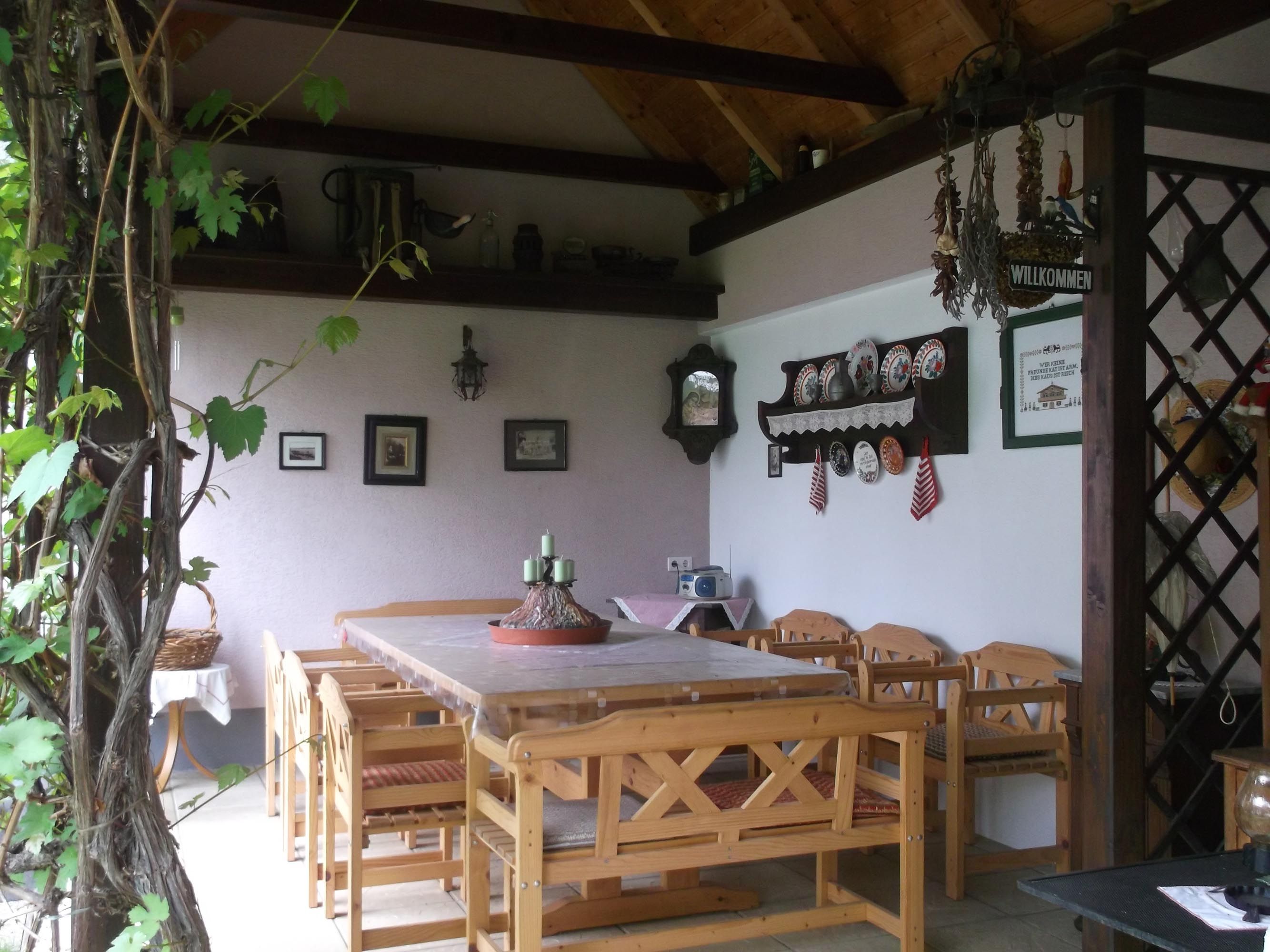 Überdachte Terasse mit Tisch und Stühlen, im Hintergrund eine Wand mit verschiedener Wanddeko.