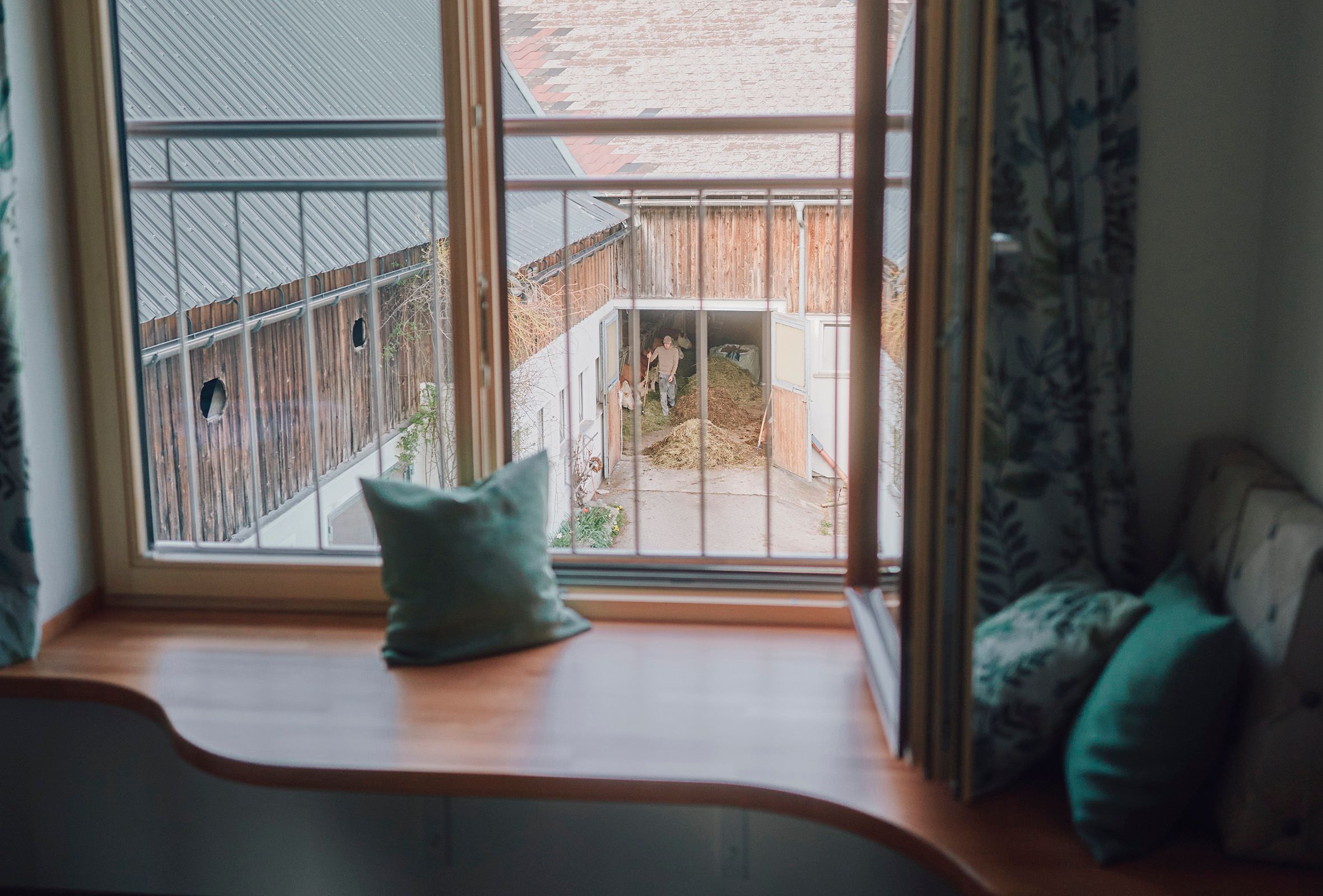 Blick aus einem Fenster auf einen Bauernhof mit einem Mann und einem Pferd im Stall.