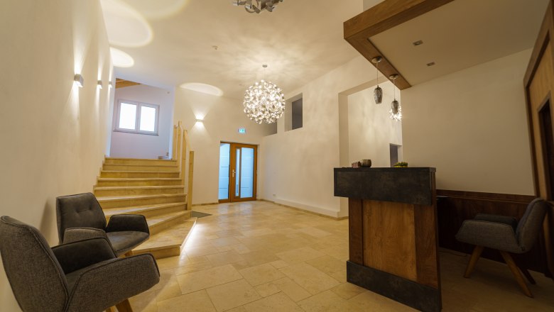 Moderne Rezeption mit Holztheke, zwei grauen Sesseln und Treppe.