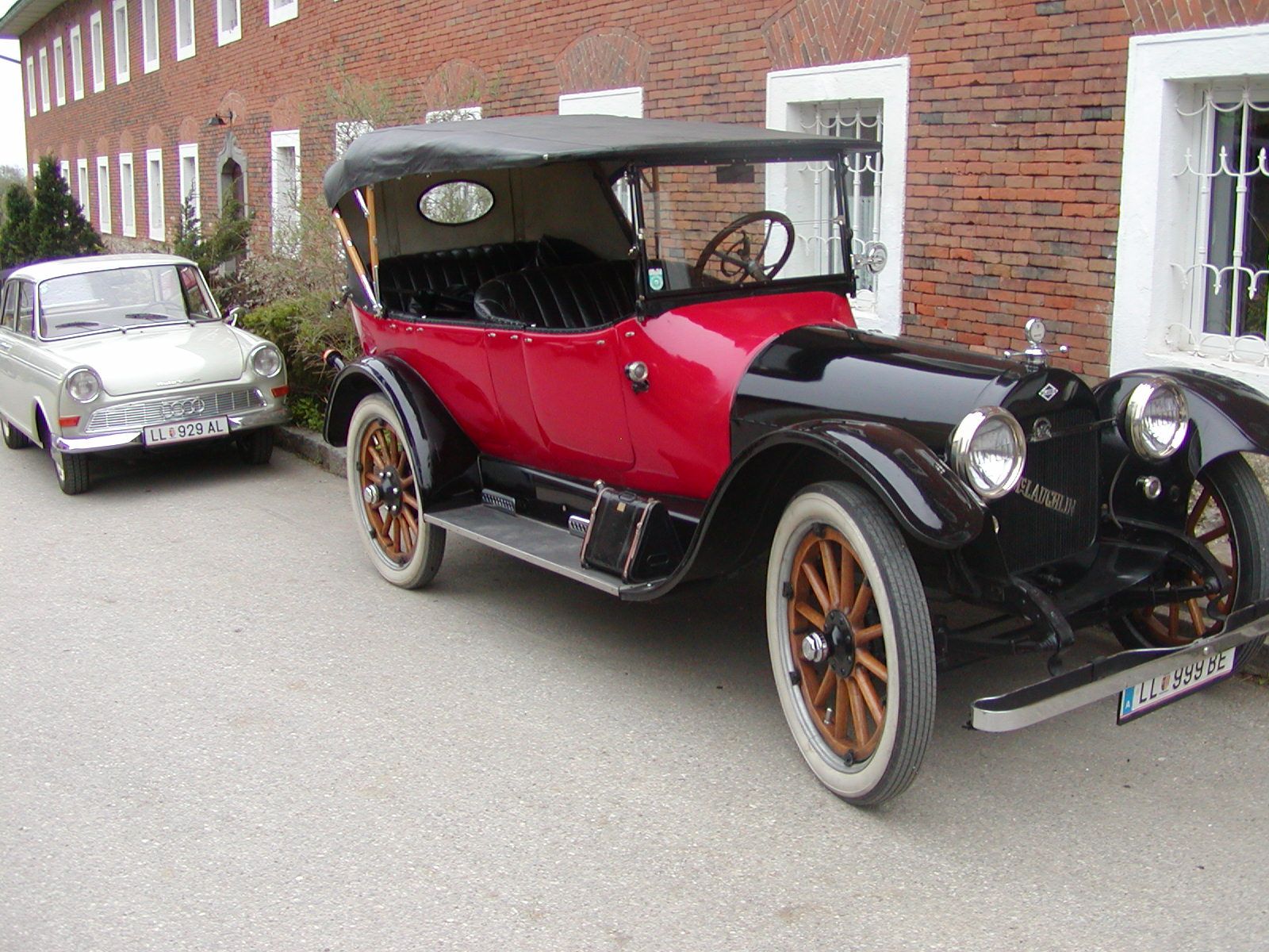 Zwei Oldtimer-Autos vor einem Backsteingebäude geparkt.