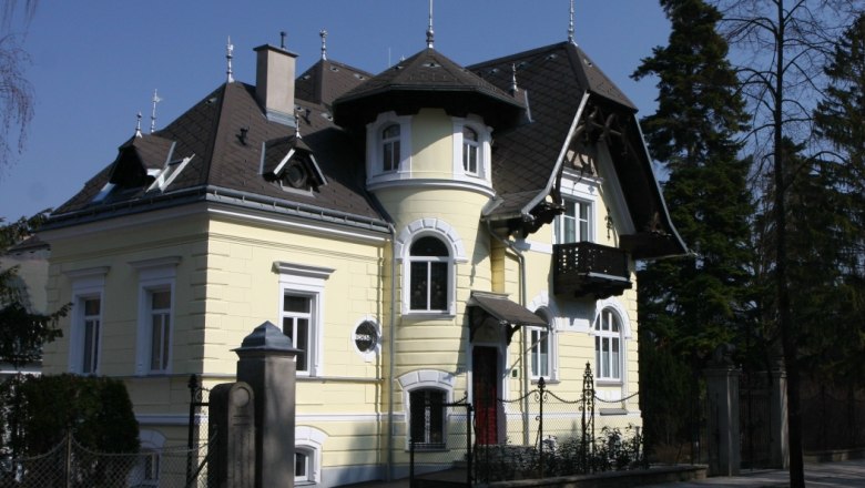 Außenansicht einer gelben Villa mit Türmchen und Balkon.