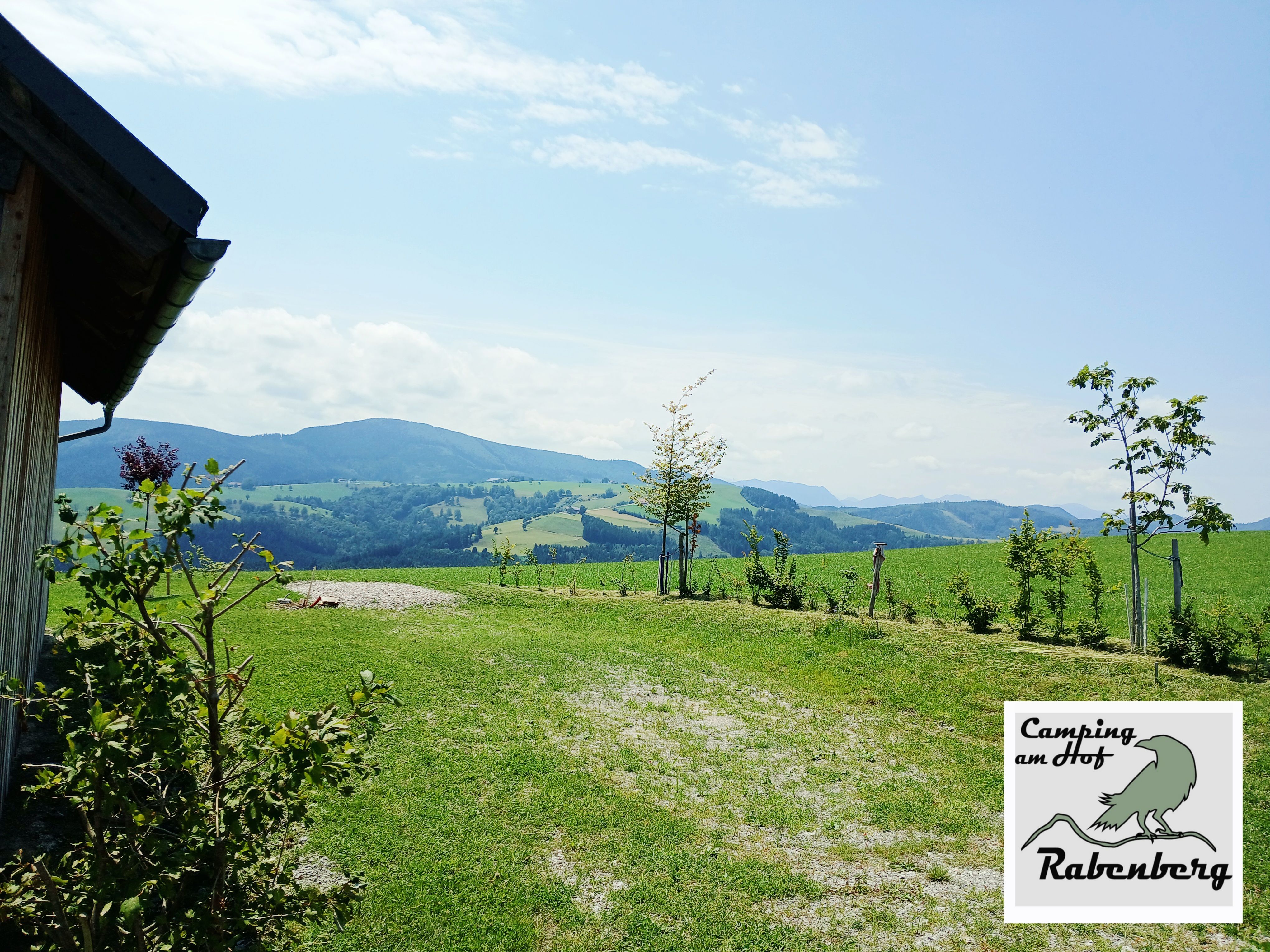 Blick von einem Stellplatz am Rabenberg auf grüne Wiesen, junge Bäume und hügelige Berge