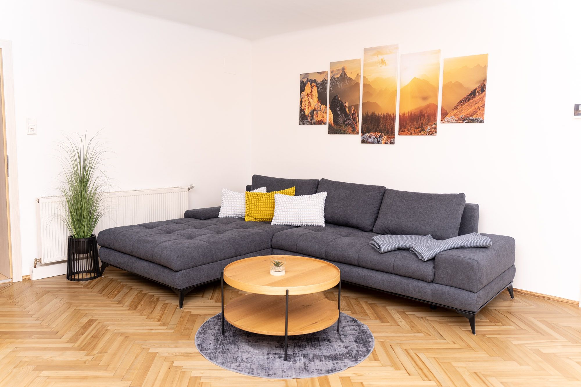 Helles Wohnzimmer der Ferienwohnung Turmblick mit grauer Eckcouch, Couchtisch, Pflanzen und Bergmotiv-Wandbildern.