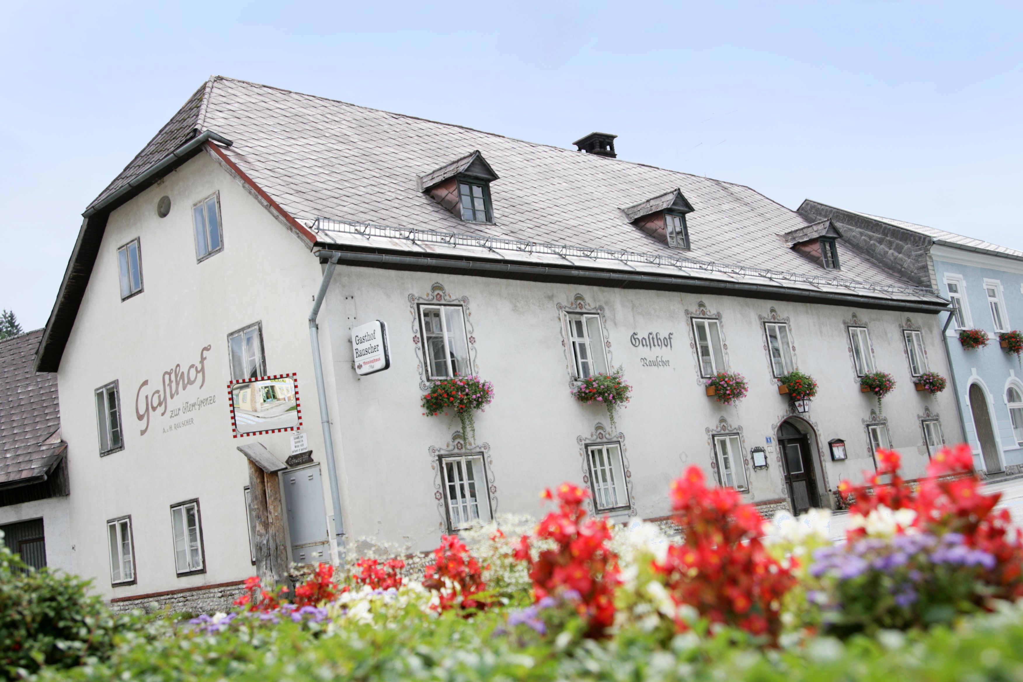 Ein traditionelles Gasthaus mit Blumen an den Fenstern und einem Schild mit der Aufschrift 'Gasthof Rauscher'.
