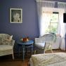 Cozy room with blue walls, two wicker armchairs, a round table with a fruit bowl and a window with white curtains.