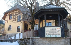 Gelbes Gästehaus mit Holzveranda und Schild 'Familie Essletzbichler Gertrude Gästezimmer'.