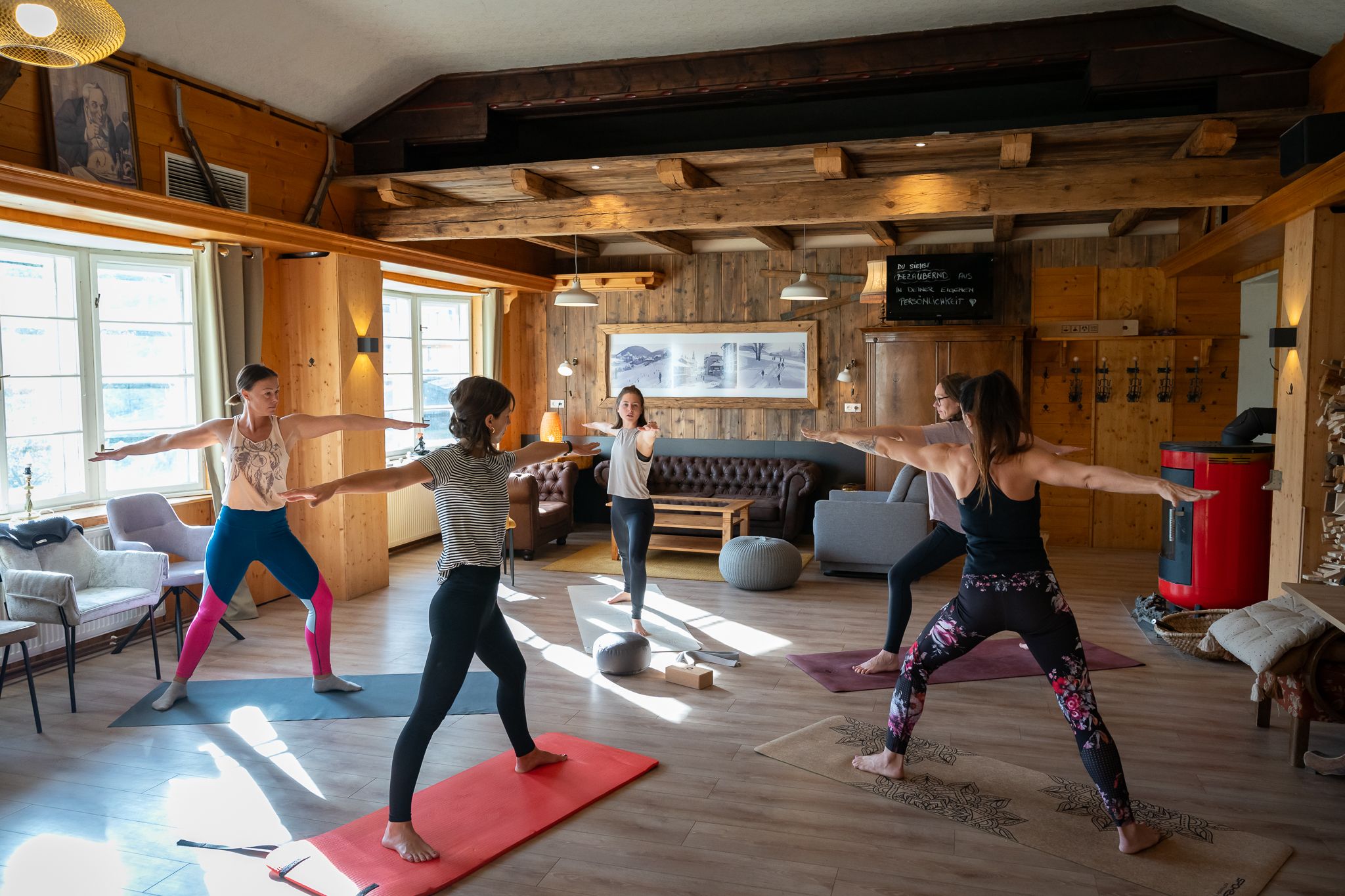 Eine Gruppe Frauen praktiziert Yoga in einem gemütlichen Raum mit Holzwänden und großen Fenstern.