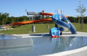 View of an aqua park with a blue children's slide and a large orange water slide in the background.