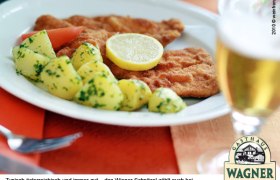 Ein Teller mit Wiener Schnitzel, Petersilienkartoffeln und einer Zitronenscheibe, daneben ein Glas Bier.