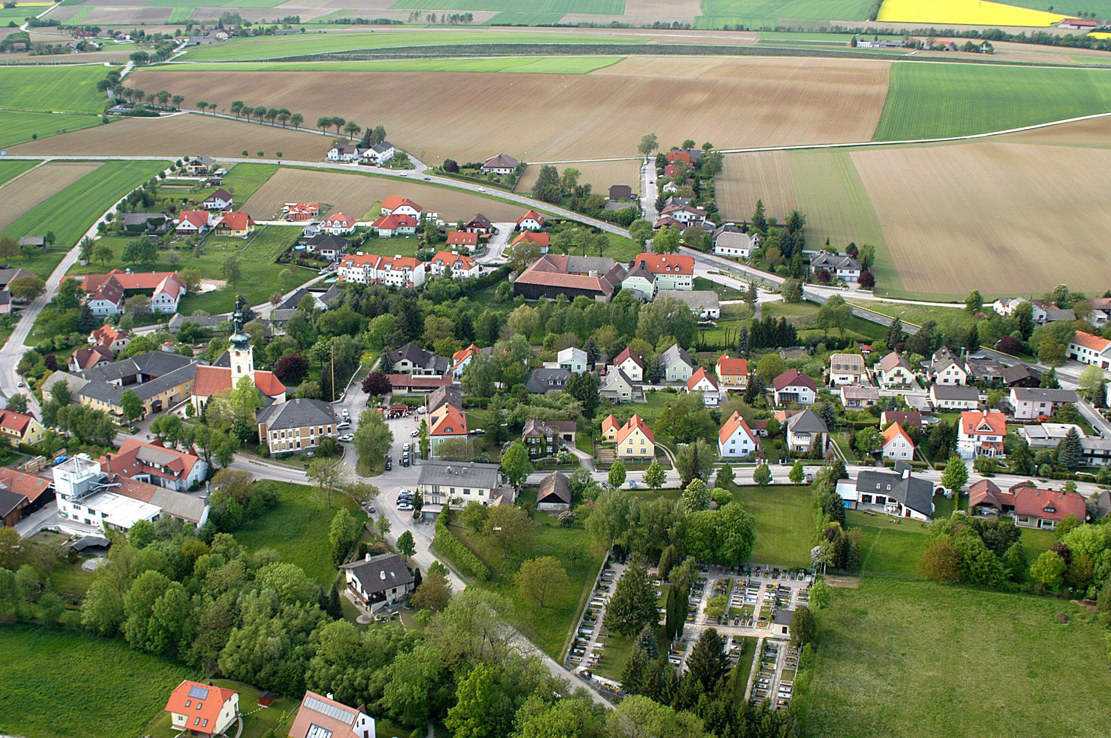 Luftaufnahme eines Dorfes mit Kirche, Wohnhäusern und Feldern.